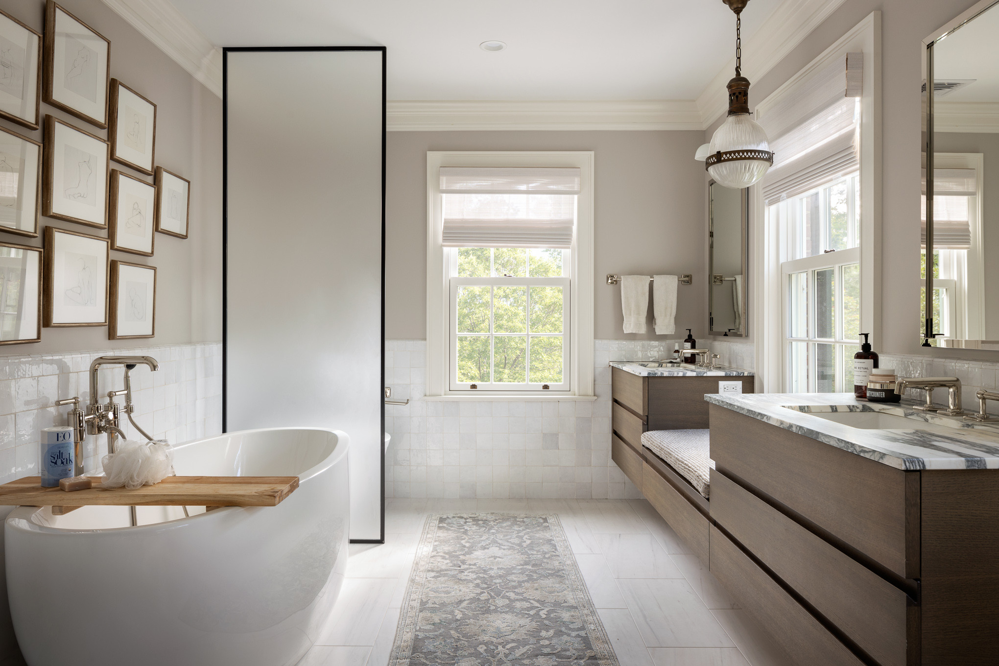 Elegant bathroom with freestanding oval tub, marble-top double vanity, and framed wall art.
