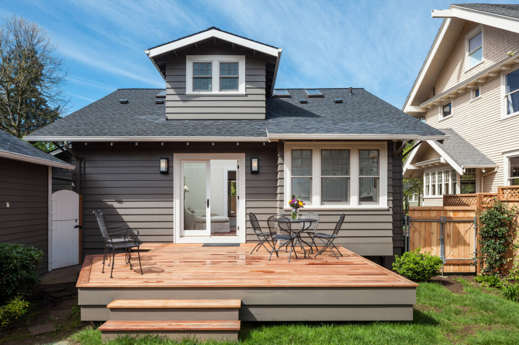 Small gray house with a new wooden deck and outdoor seating area.