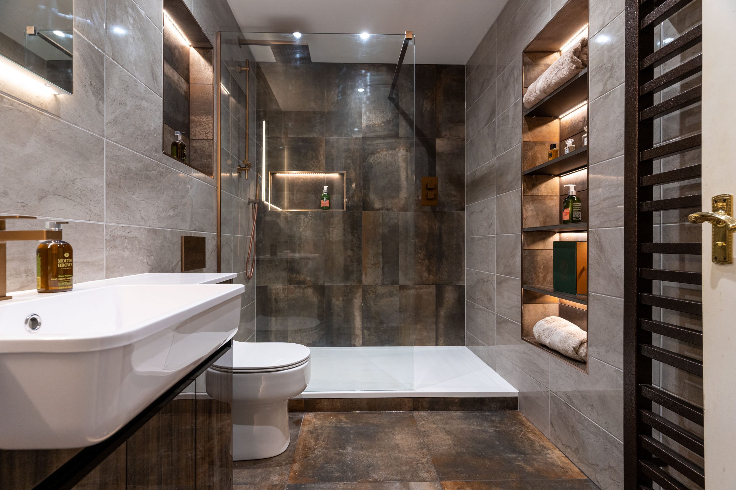 Modern bathroom with a walk-in shower, built-in shelving, and warm-toned tiles.