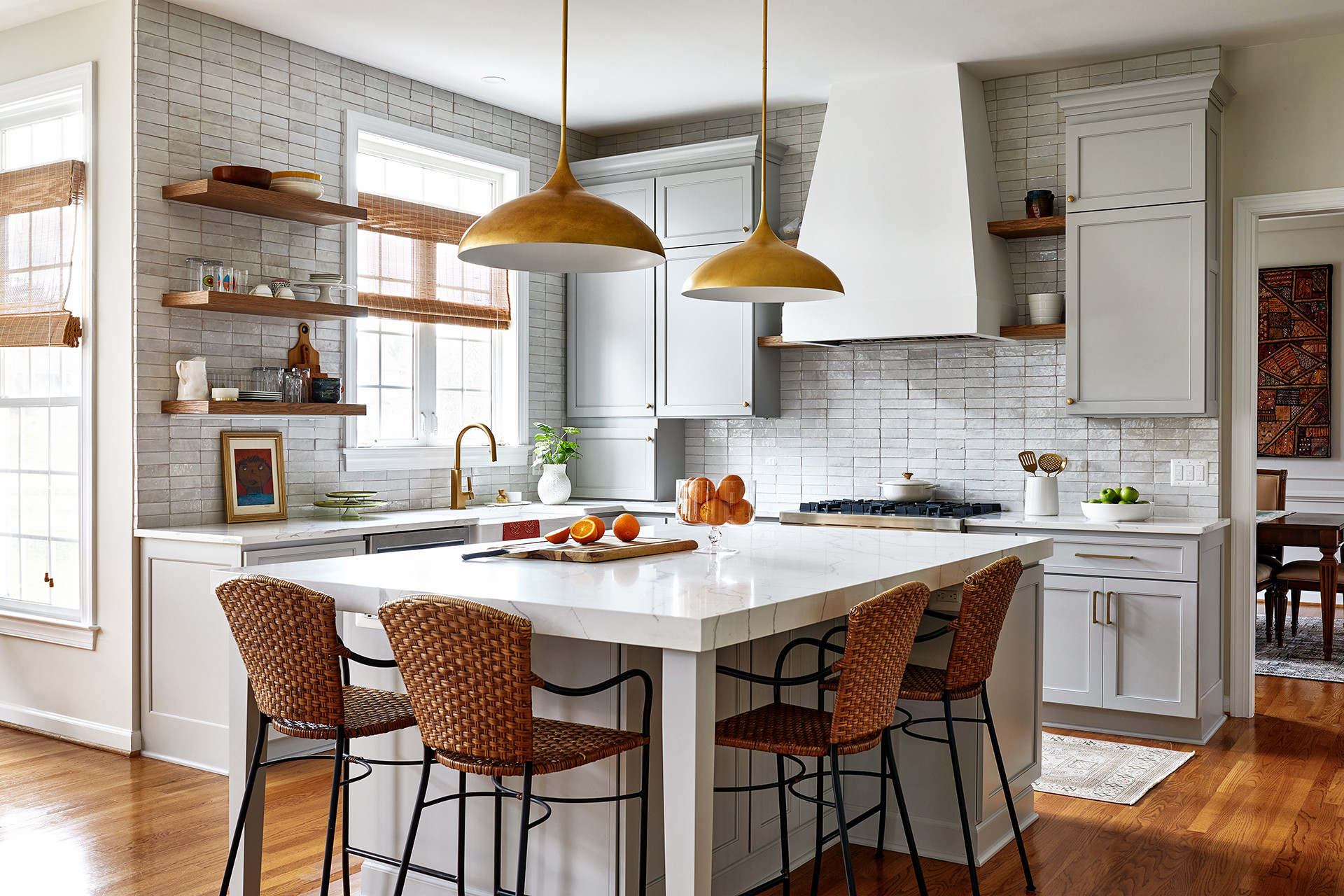 Modern kitchen with gray cabinetry, gold pendant lights, and a white marble island with woven bar stools.