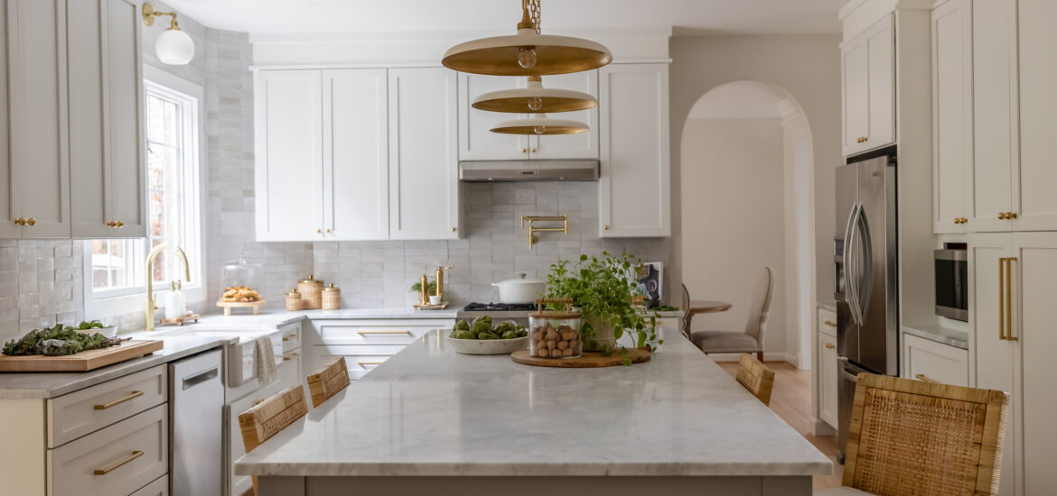 Bright kitchen with white cabinetry, gold accents, and a large marble island with rattan bar stools.