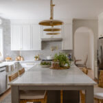 Bright kitchen with white cabinetry, gold accents, and a large marble island with rattan bar stools.