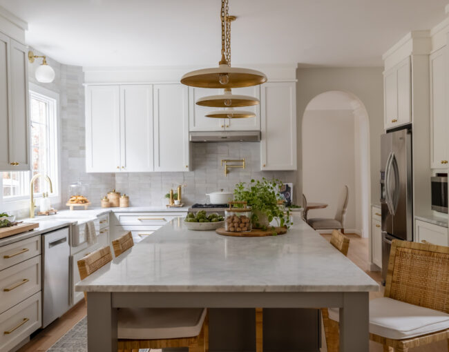 Bright kitchen with white cabinetry, gold accents, and a large marble island with rattan bar stools.