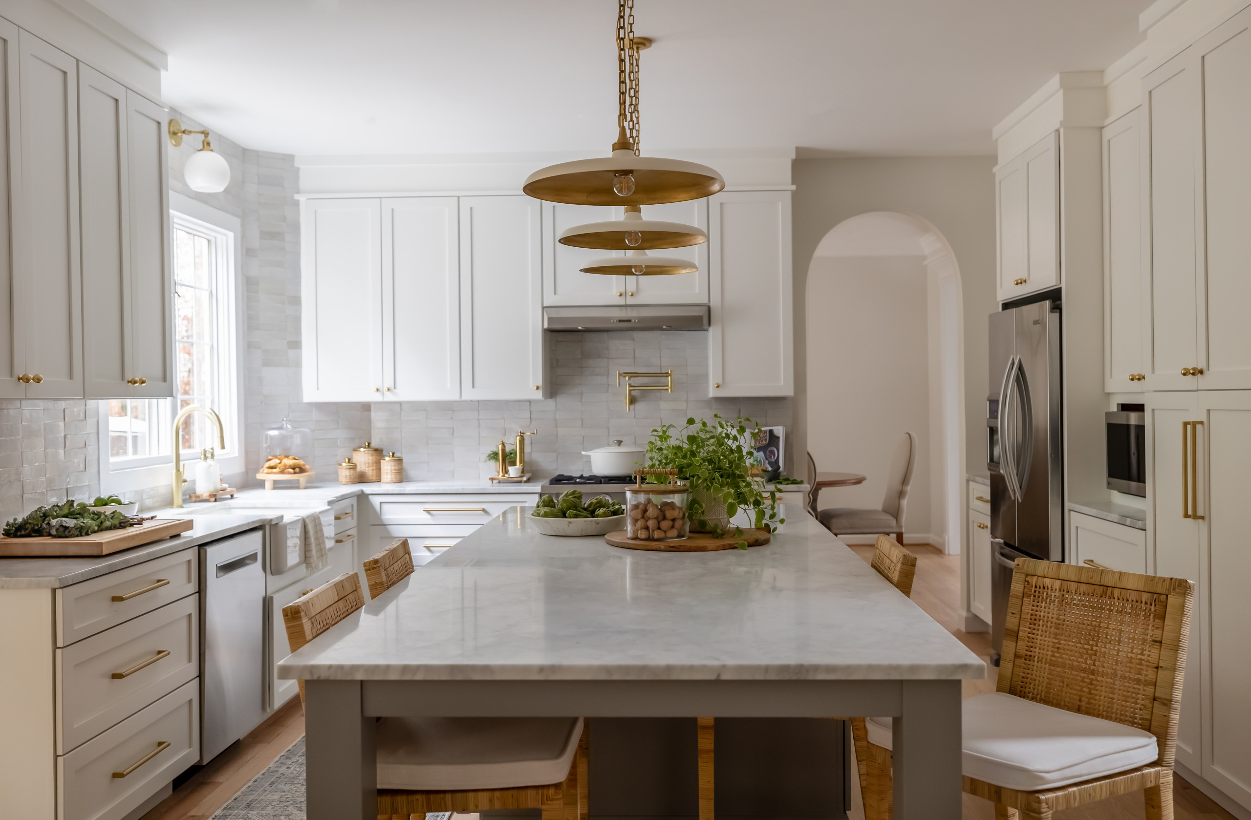 Bright kitchen with white cabinetry, gold accents, and a large marble island with rattan bar stools.