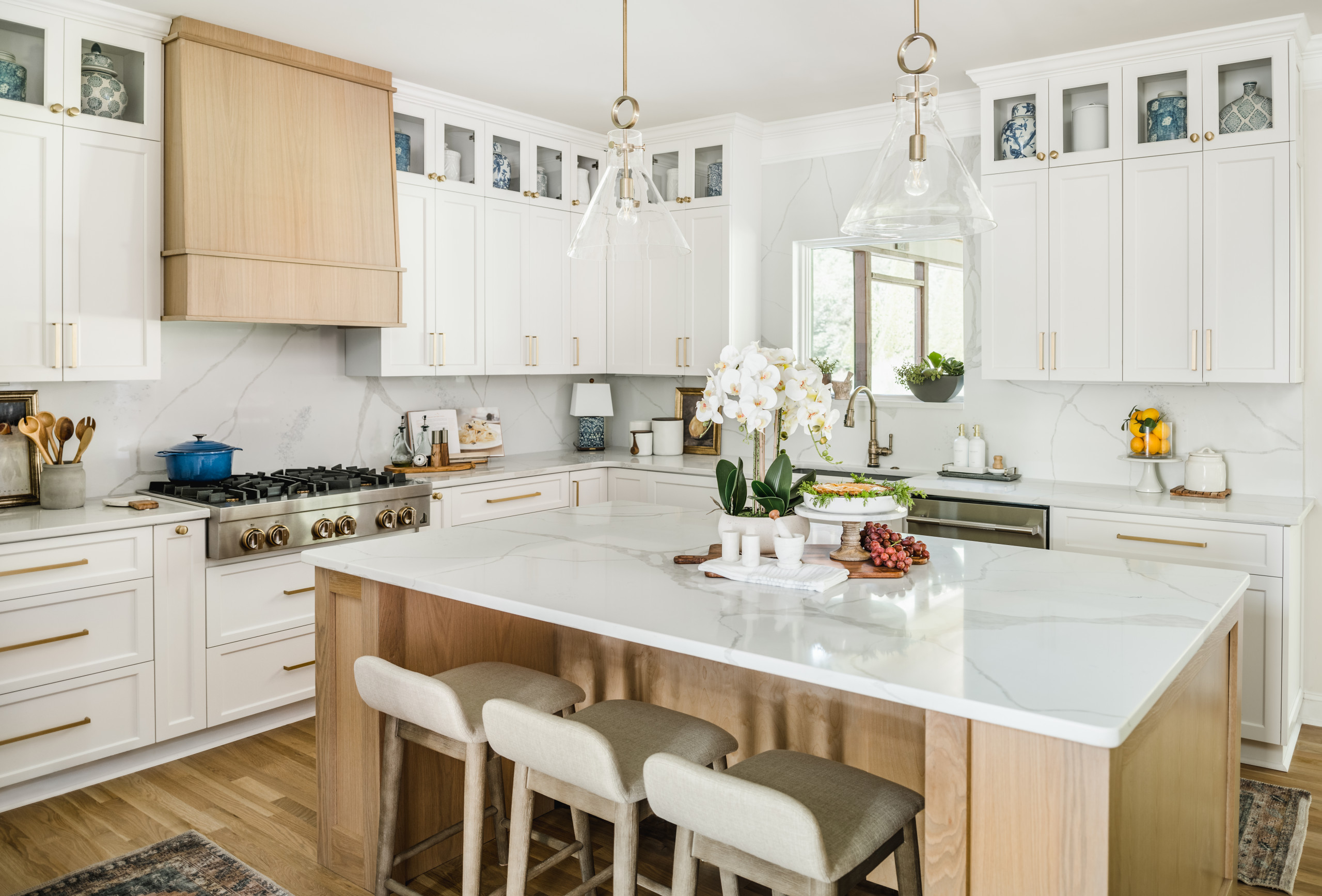 Bright kitchen with white shaker cabinets, gold hardware, and a large marble island with light wood accents and upholstered stools.