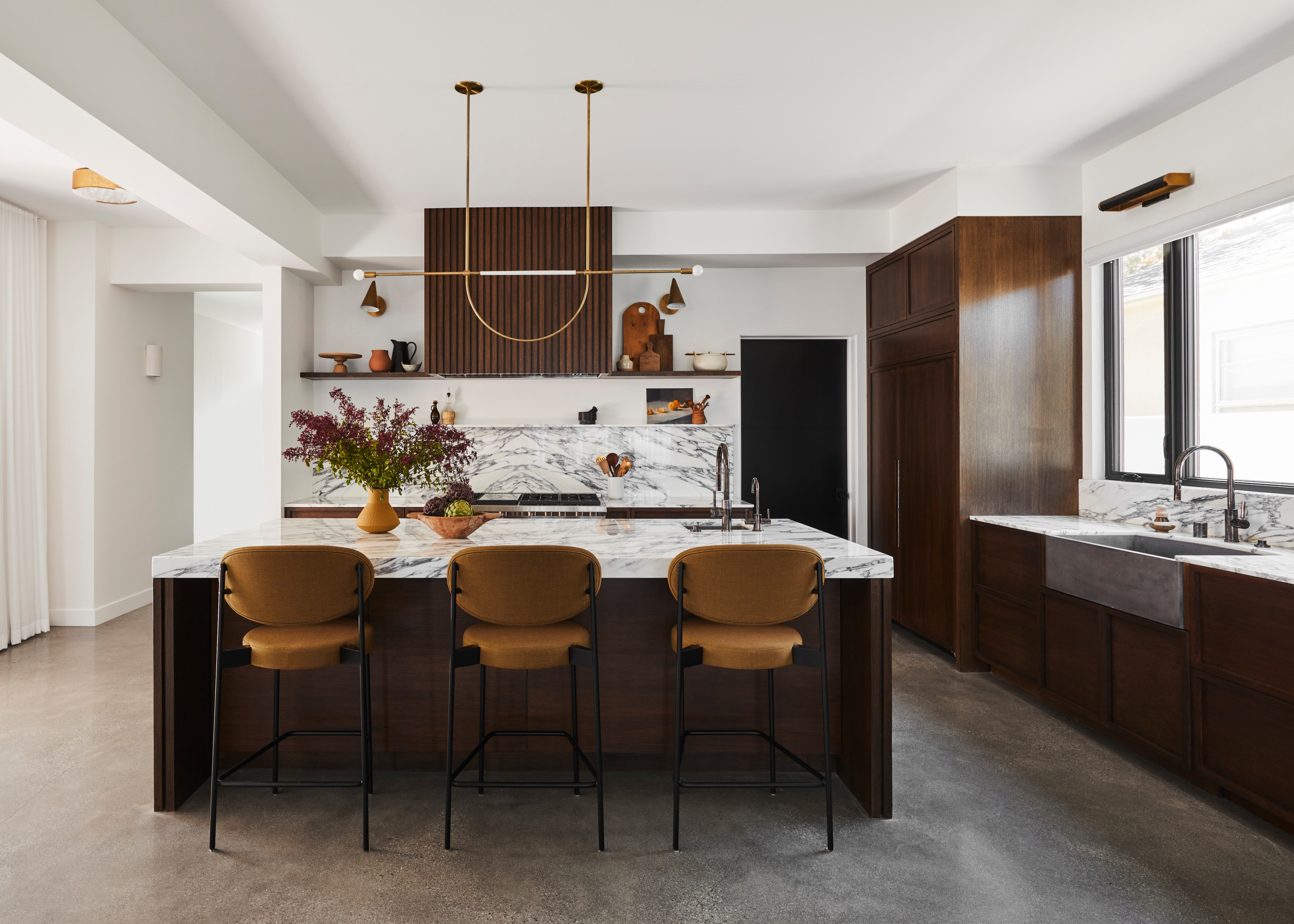 Contemporary kitchen with rich dark wood cabinetry, marble countertops, and gold-accented lighting.