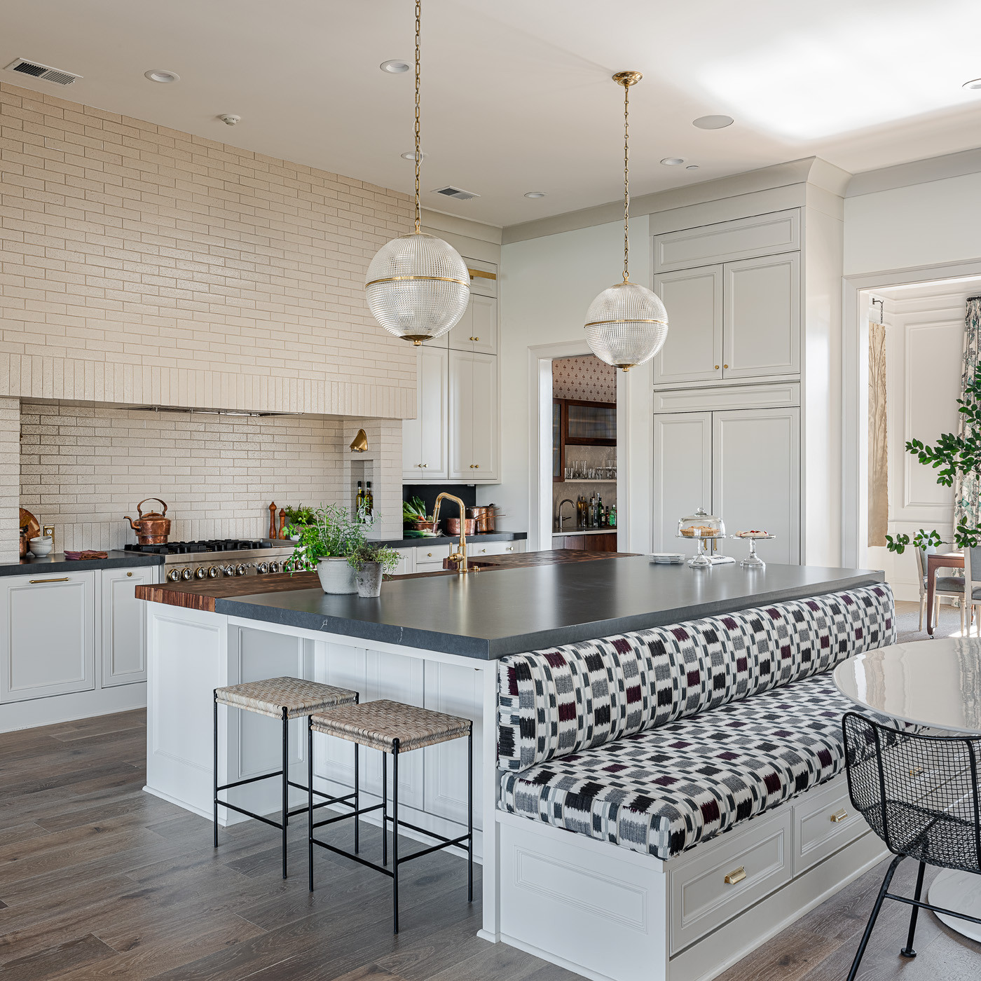 Elegant kitchen with large black countertop island, built-in patterned bench seating, and globe pendant lighting.