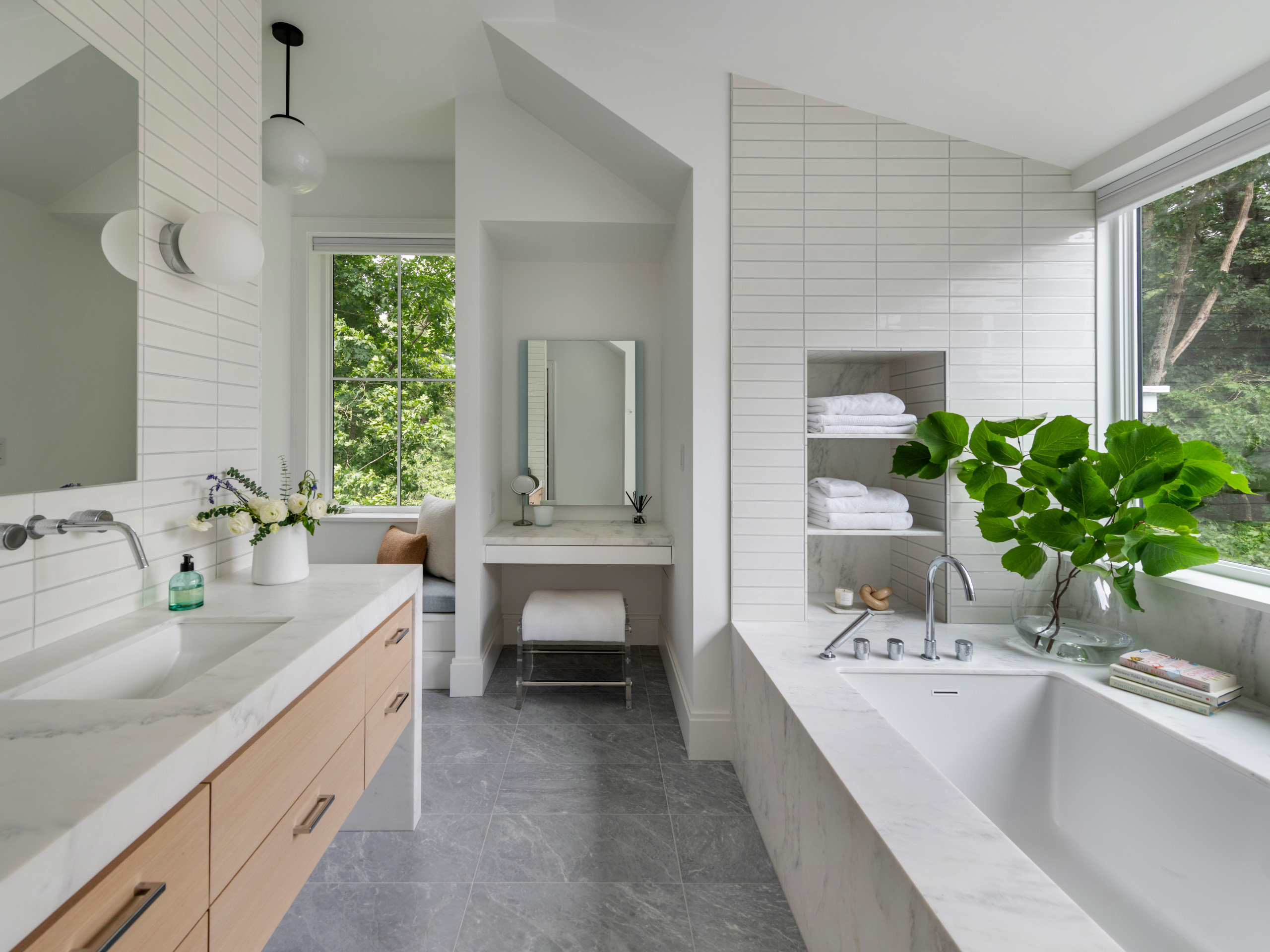 Modern bathroom with a built-in bathtub, light wood vanity, and large windows overlooking greenery.
