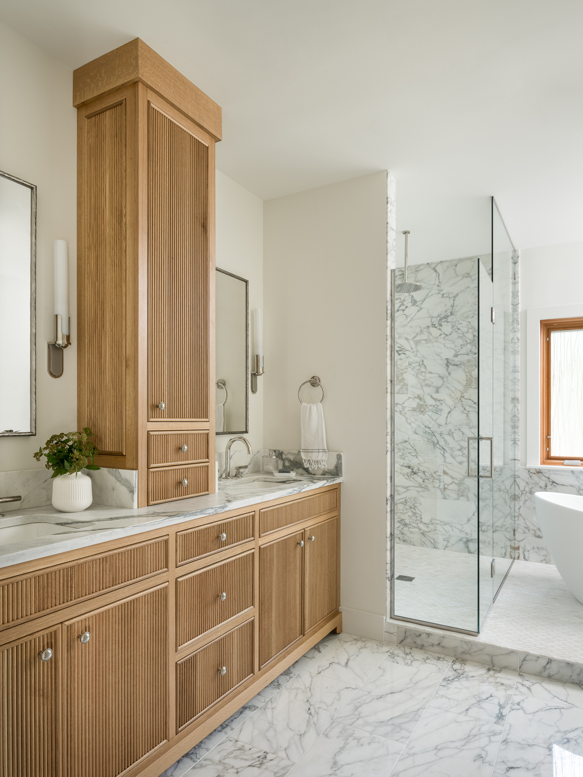Elegant bathroom with marble flooring, wood vanity, and glass-enclosed shower.