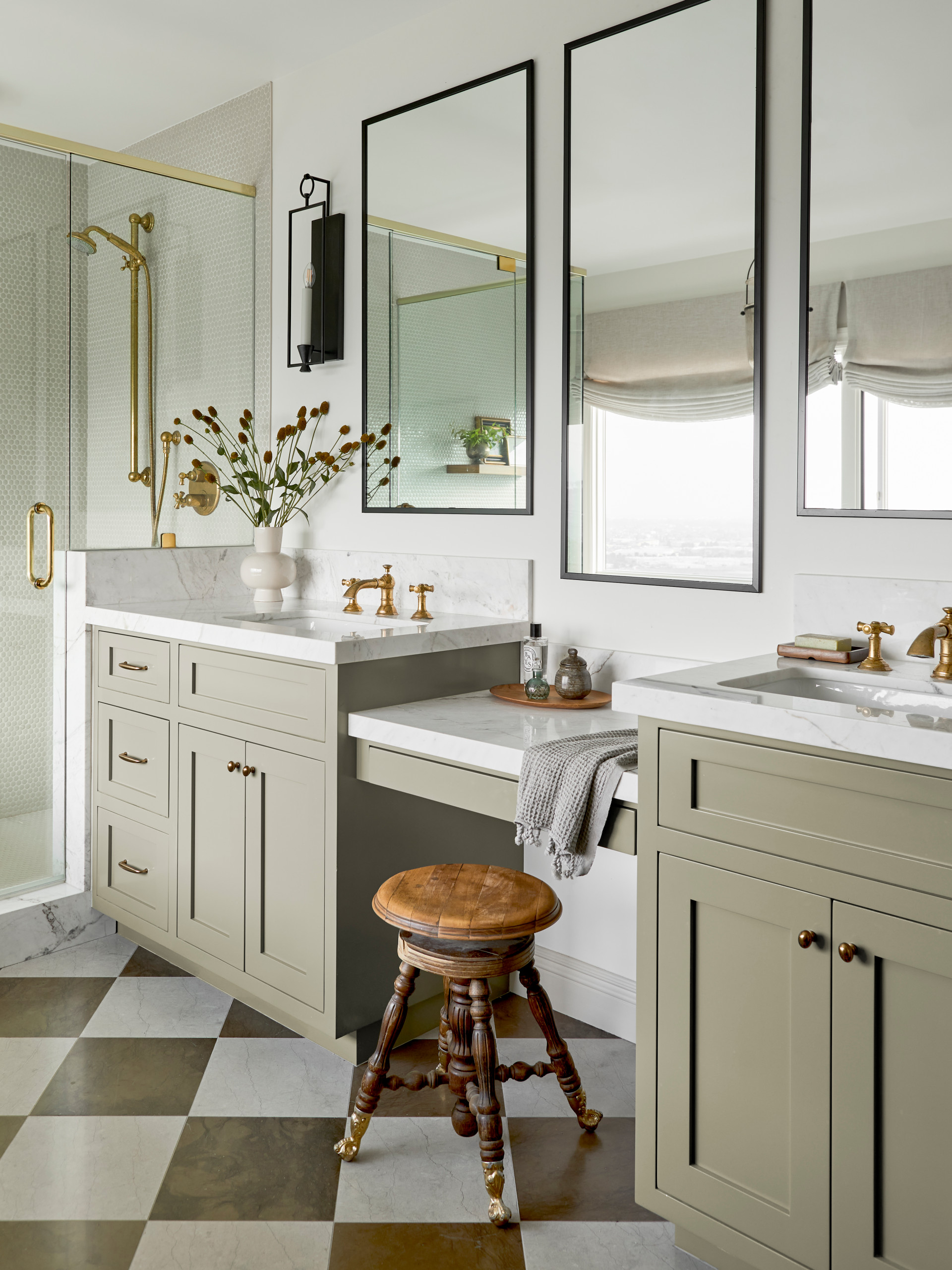 Elegant bathroom with sage green cabinets, marble countertops, gold fixtures, and a checkered marble floor.