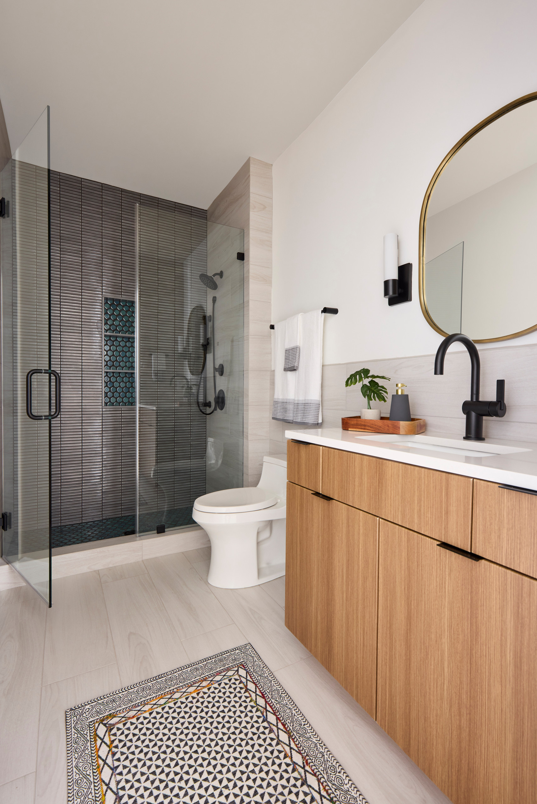 Modern bathroom with glass-enclosed shower, wood vanity, and geometric floor rug.