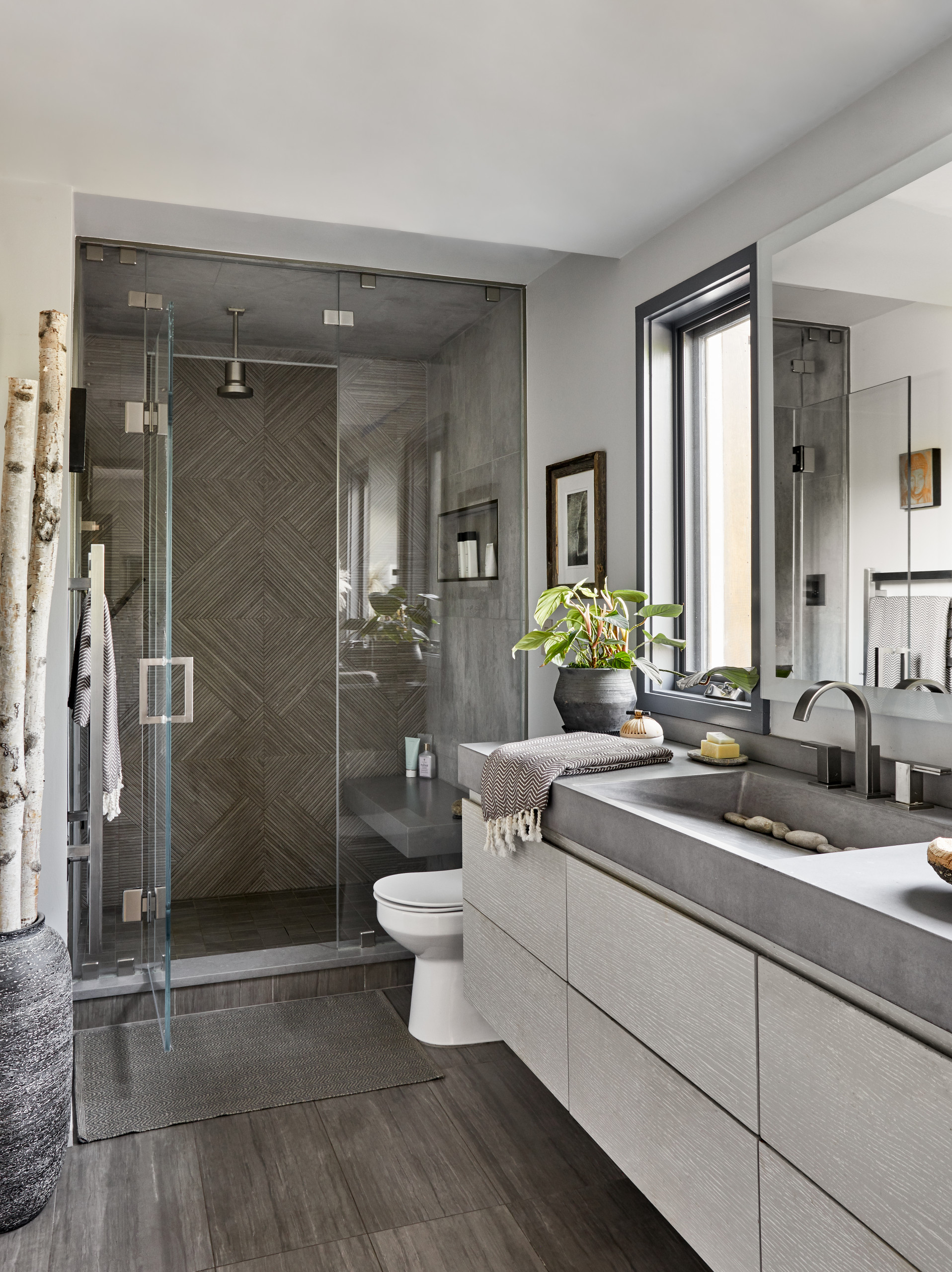 Modern bathroom with glass shower, patterned tile wall, and concrete vanity.