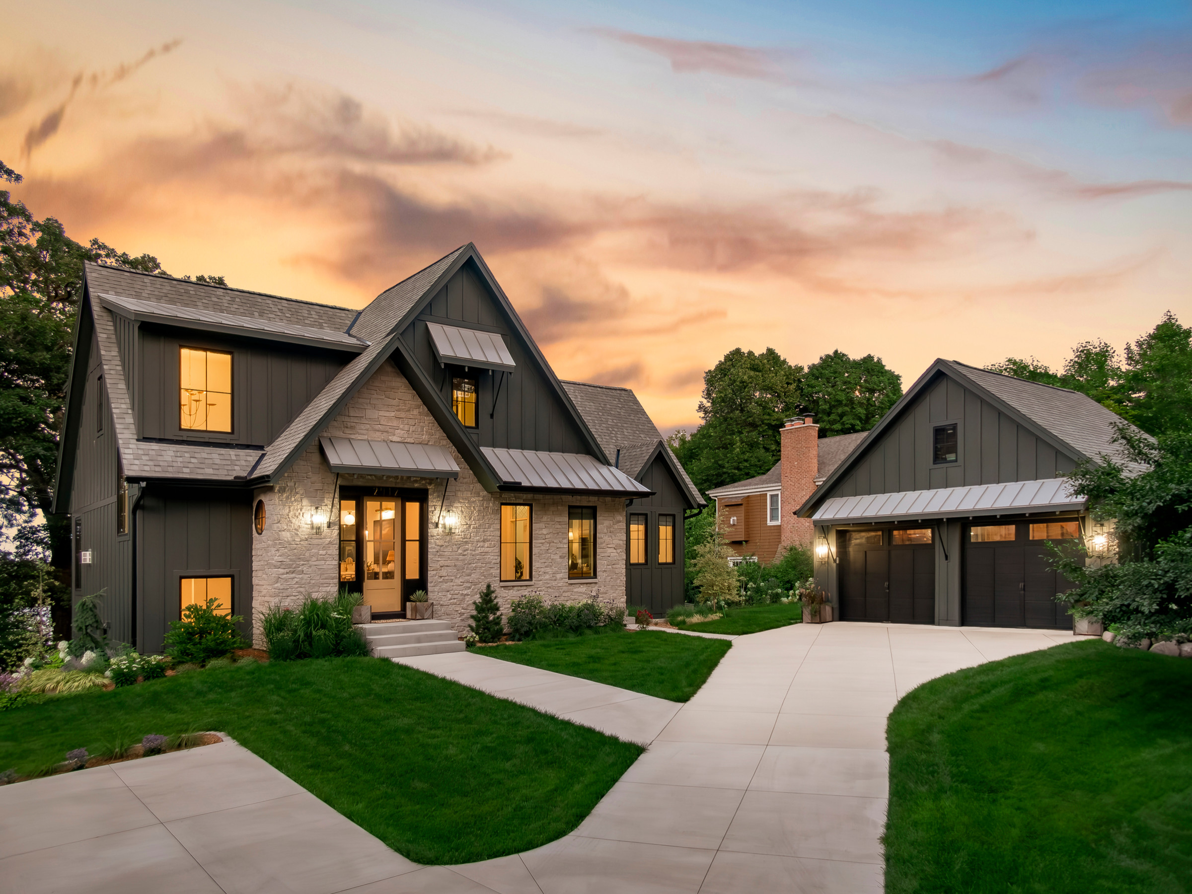 Modern farmhouse-style home with stone and dark siding exterior, illuminated at sunset.