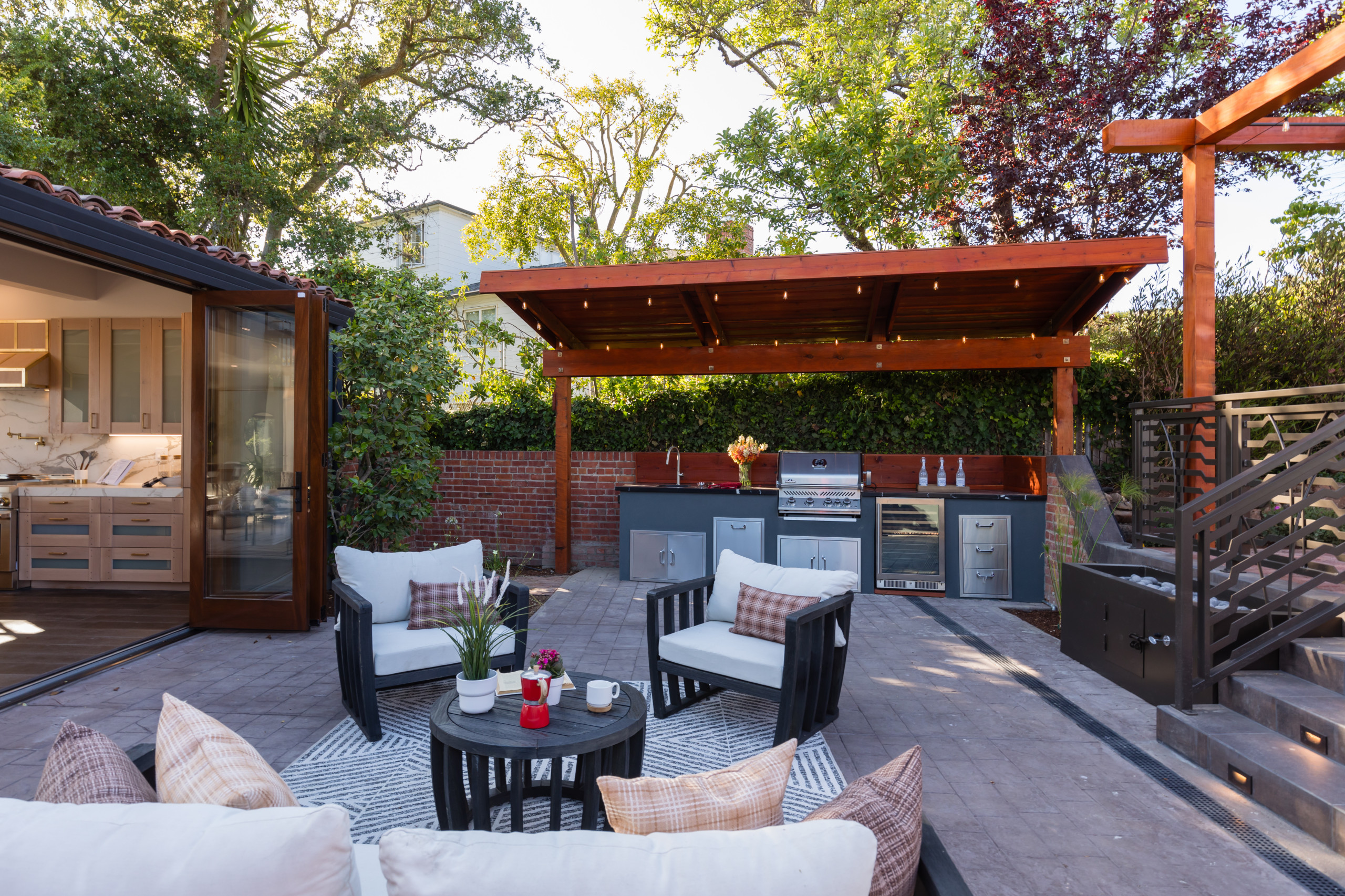 Modern outdoor kitchen and seating area with a pergola, grill station, and comfortable seating.