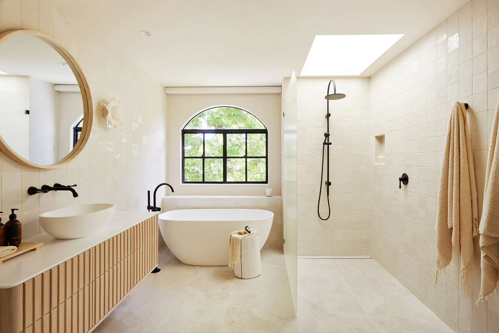 Modern bathroom with freestanding tub, open shower, and arched window.