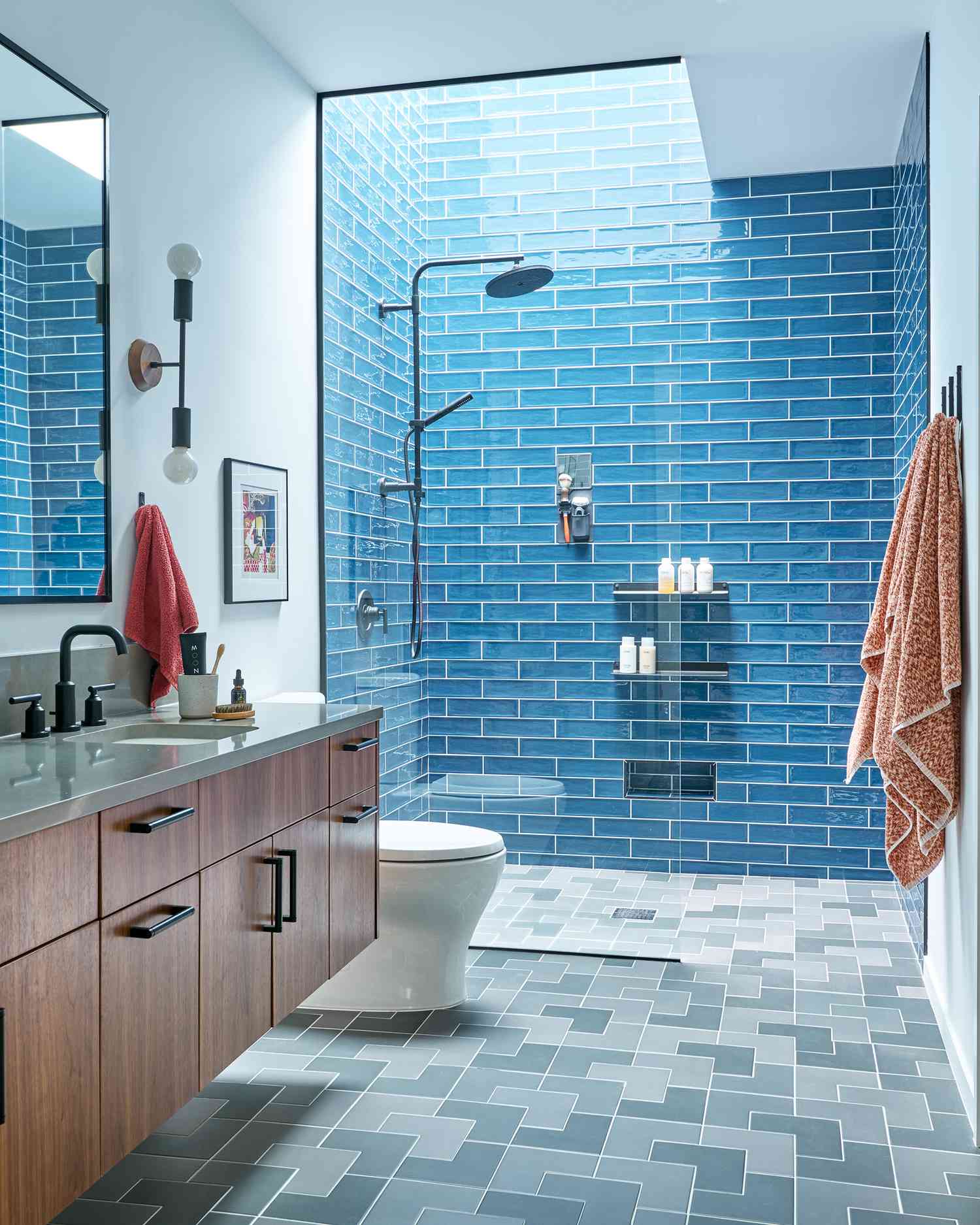 Modern bathroom with bold blue subway tile shower, floating wood vanity, and geometric gray floor tiles.