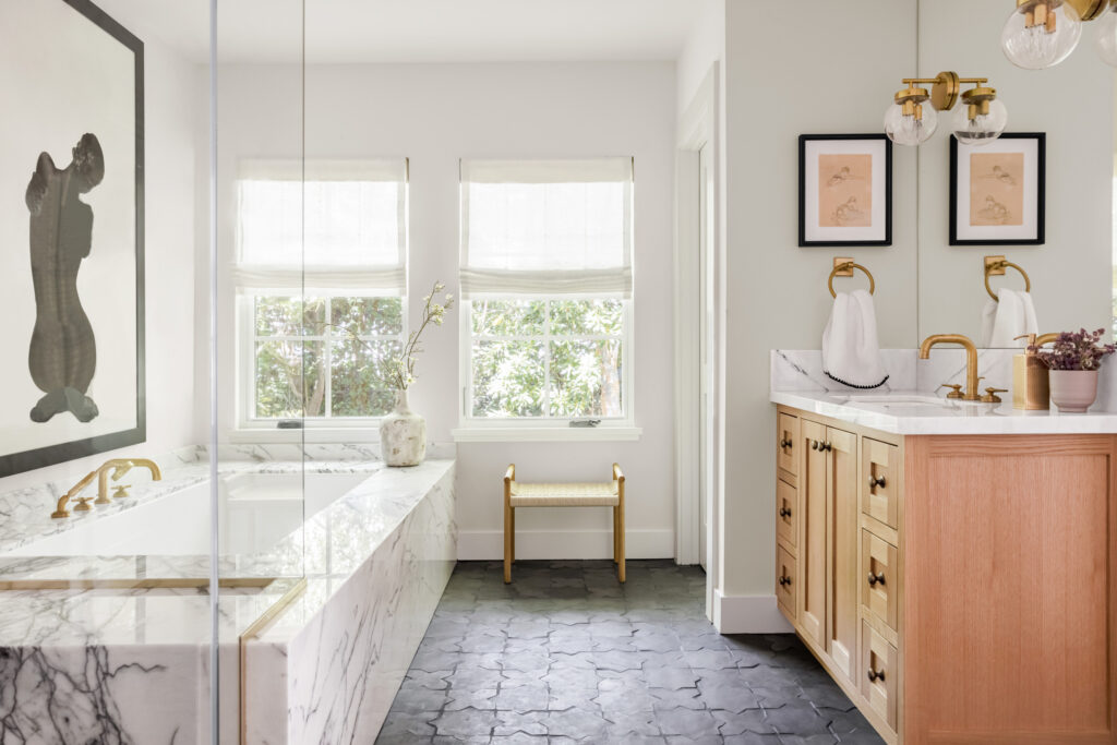 Bright bathroom with marble tub, light wood vanity, and gold fixtures