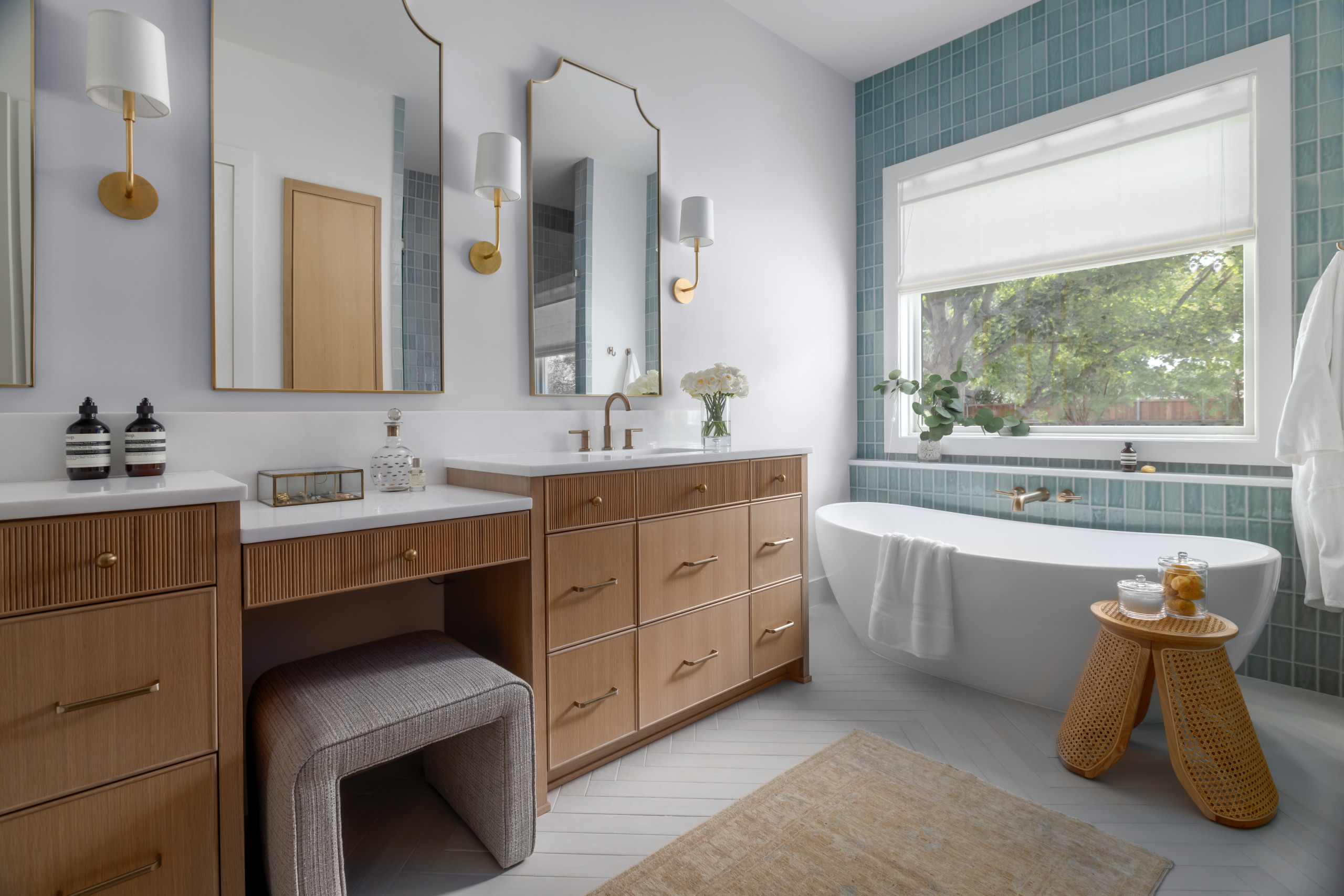 Modern bathroom with wooden vanity, gold fixtures, freestanding bathtub, and teal tile accent wall.