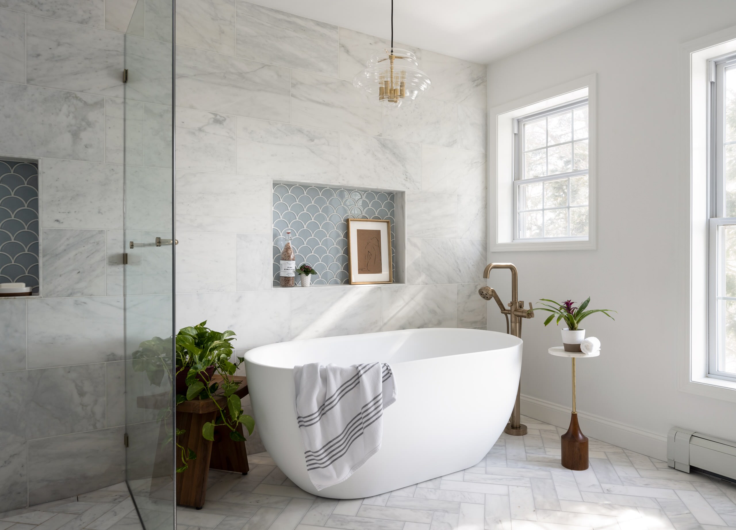 Modern bathroom with freestanding bathtub, marble walls, and built-in niche with blue scallop tiles.