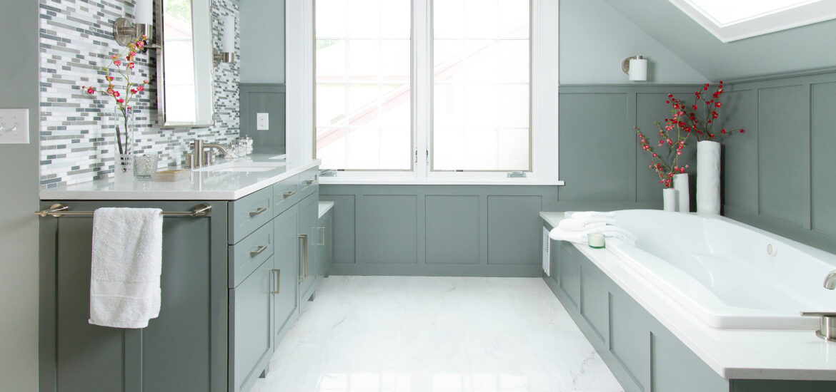 Elegant bathroom with green cabinetry, built-in bathtub, and mosaic tile backsplash.