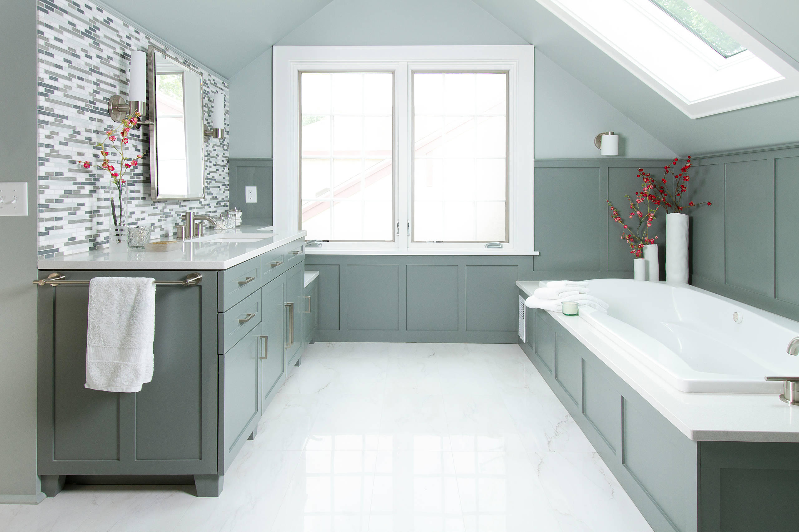 Elegant bathroom with green cabinetry, built-in bathtub, and mosaic tile backsplash.