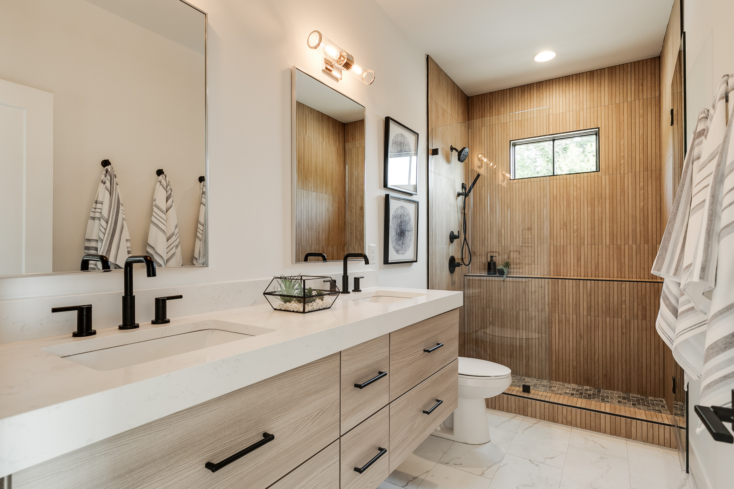 Modern bathroom with double vanity, black fixtures, and a walk-in shower with wood-style tile walls.