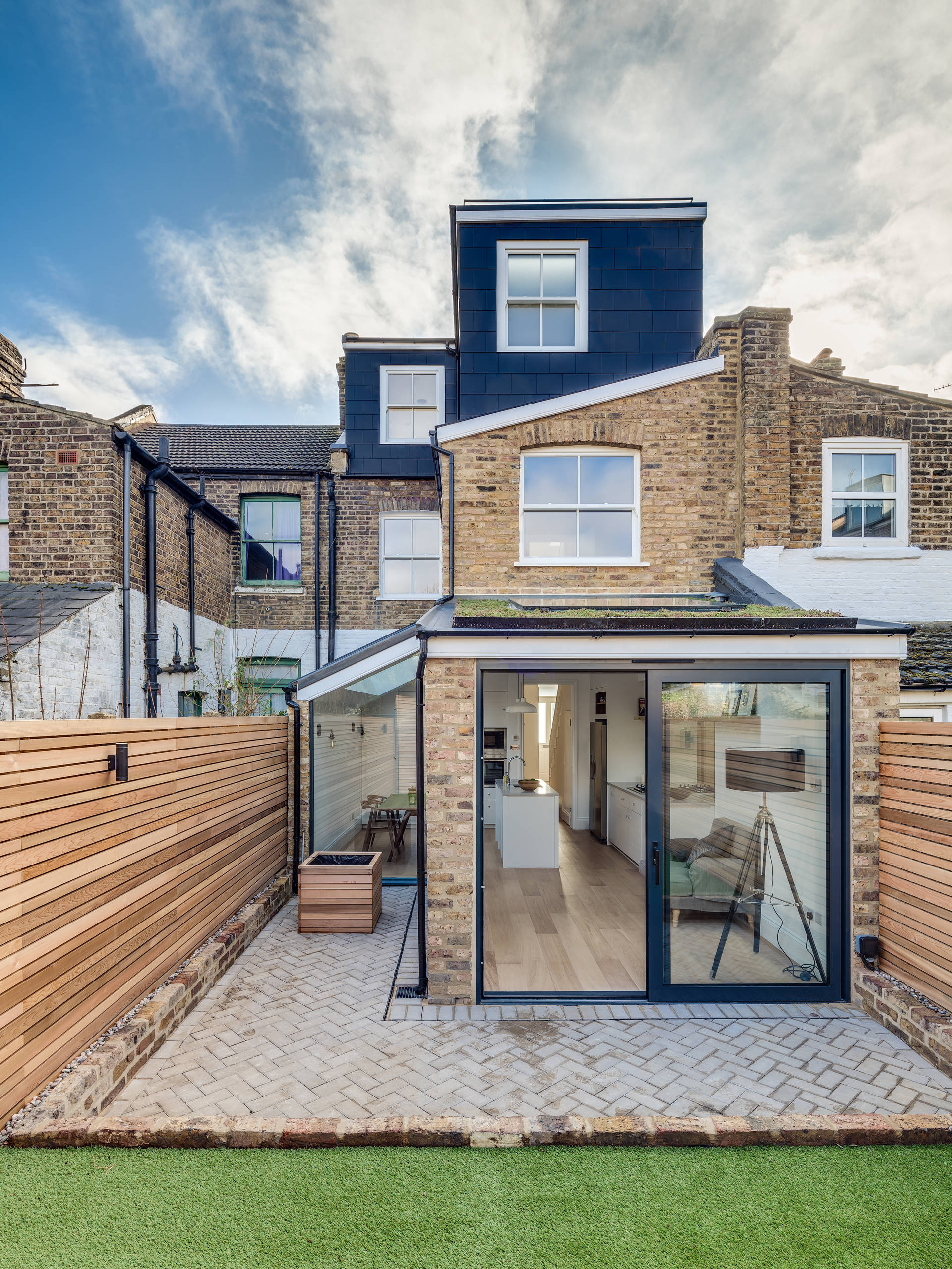 Modern brick townhouse with a glass extension and wooden fence in the backyard.