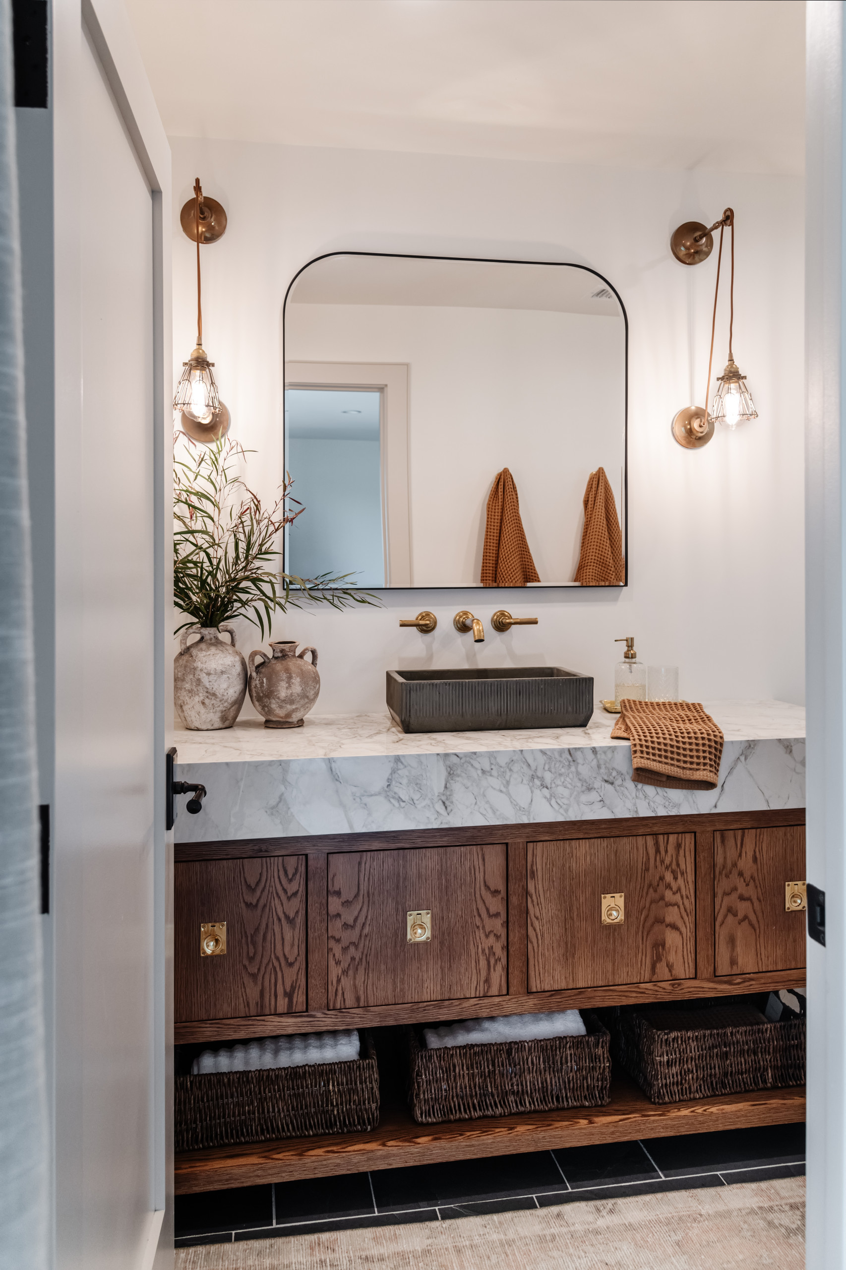 Rustic modern bathroom with marble countertop, vessel sink, and brass fixtures.
