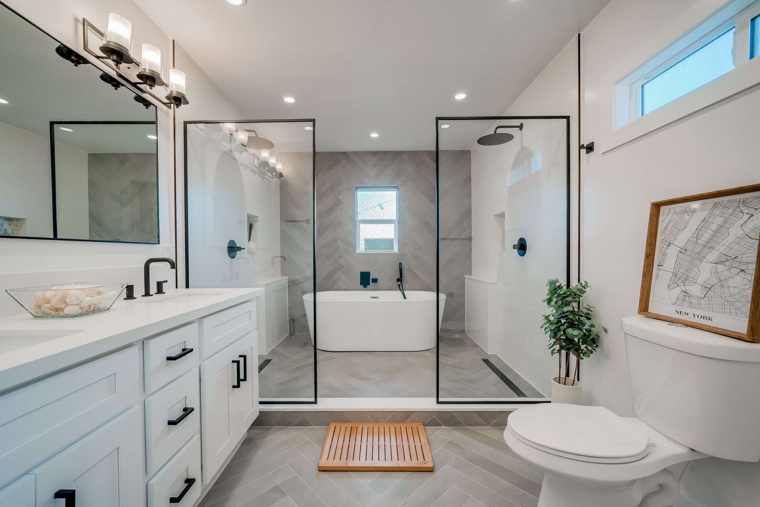 Modern bathroom with glass-enclosed shower, freestanding bathtub, and white vanity with black hardware.