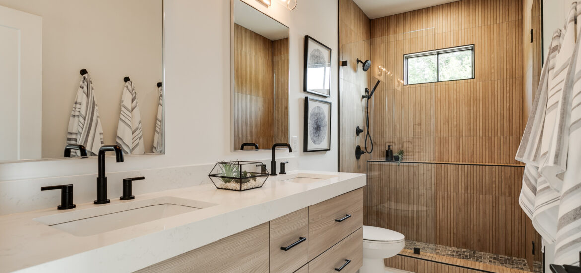Modern bathroom with wood-accent shower, double vanity, and black fixtures.