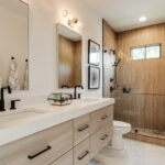 Modern bathroom with wood-accent shower, double vanity, and black fixtures.