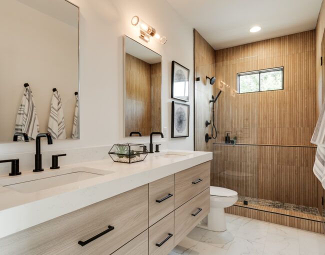 Modern bathroom with wood-accent shower, double vanity, and black fixtures.
