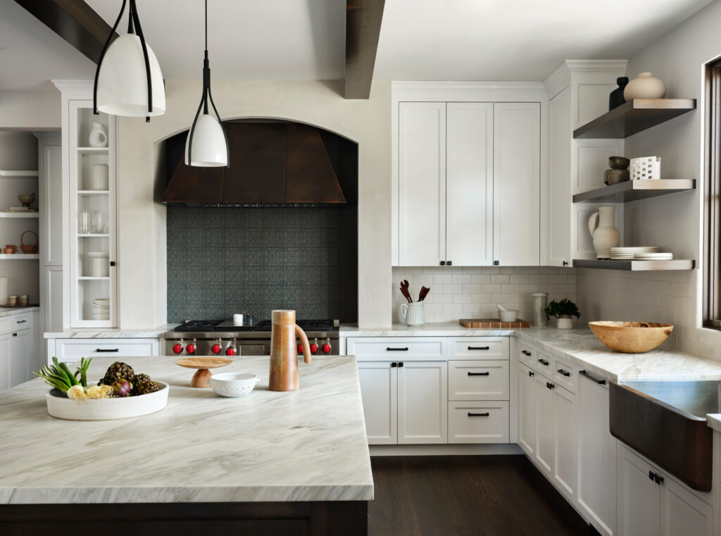Modern kitchen with marble countertops, white cabinetry, and black tile backsplash.