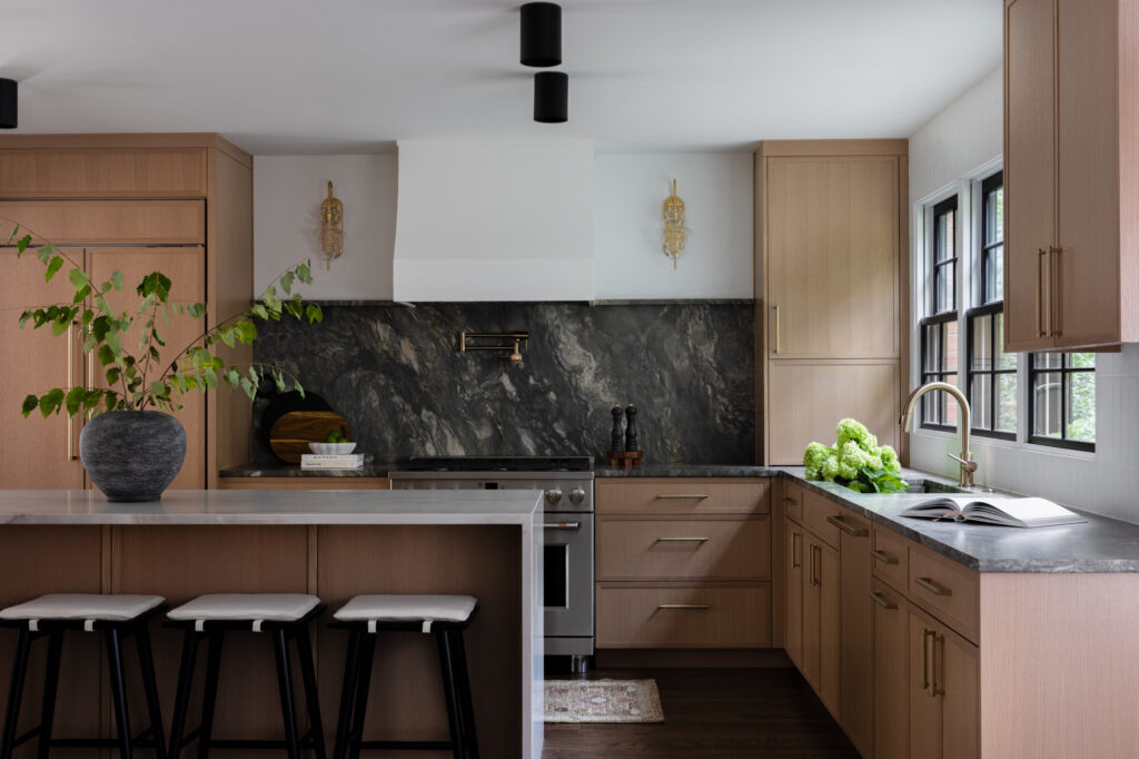 Modern kitchen with light wood cabinetry, dark marble backsplash, and waterfall island.