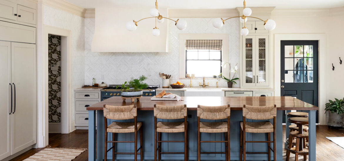 Spacious kitchen with large wooden island, woven bar stools, and modern brass light fixtures.