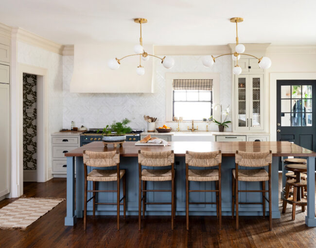 Spacious kitchen with large wooden island, woven bar stools, and modern brass light fixtures.