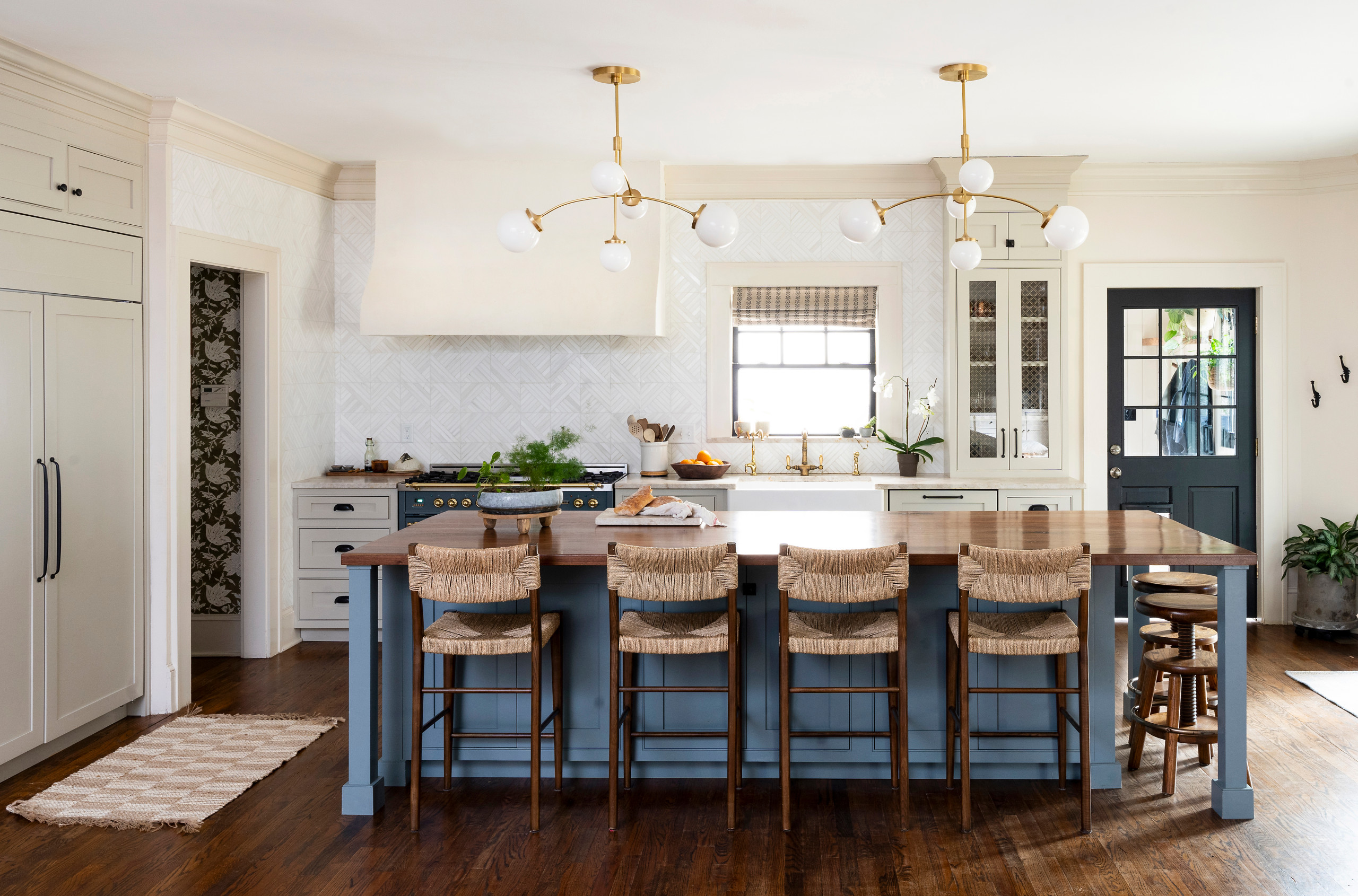 Spacious kitchen with large wooden island, woven bar stools, and modern brass light fixtures.
