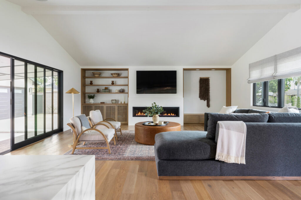 Modern living room with sectional sofa, built-in shelves, and fireplace beneath mounted TV.