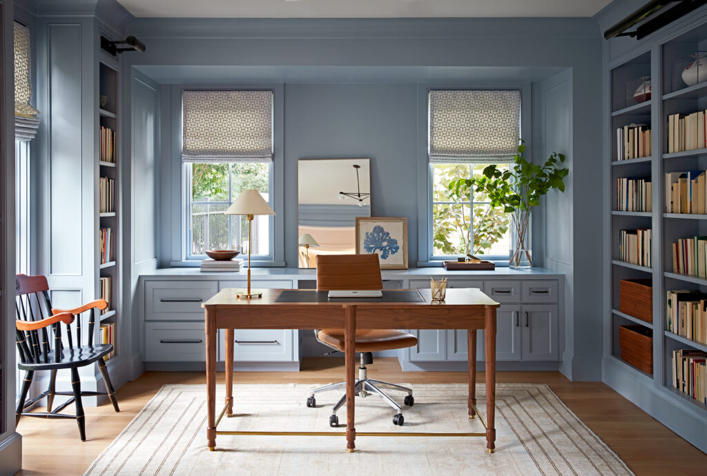 Elegant home office with blue built-in bookshelves, wooden desk, and large windows.