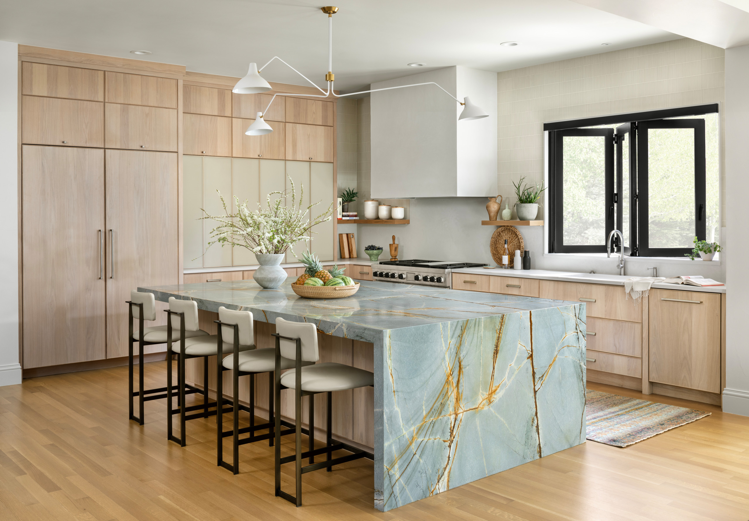 Modern kitchen with a large blue quartzite waterfall island and light wood cabinetry.