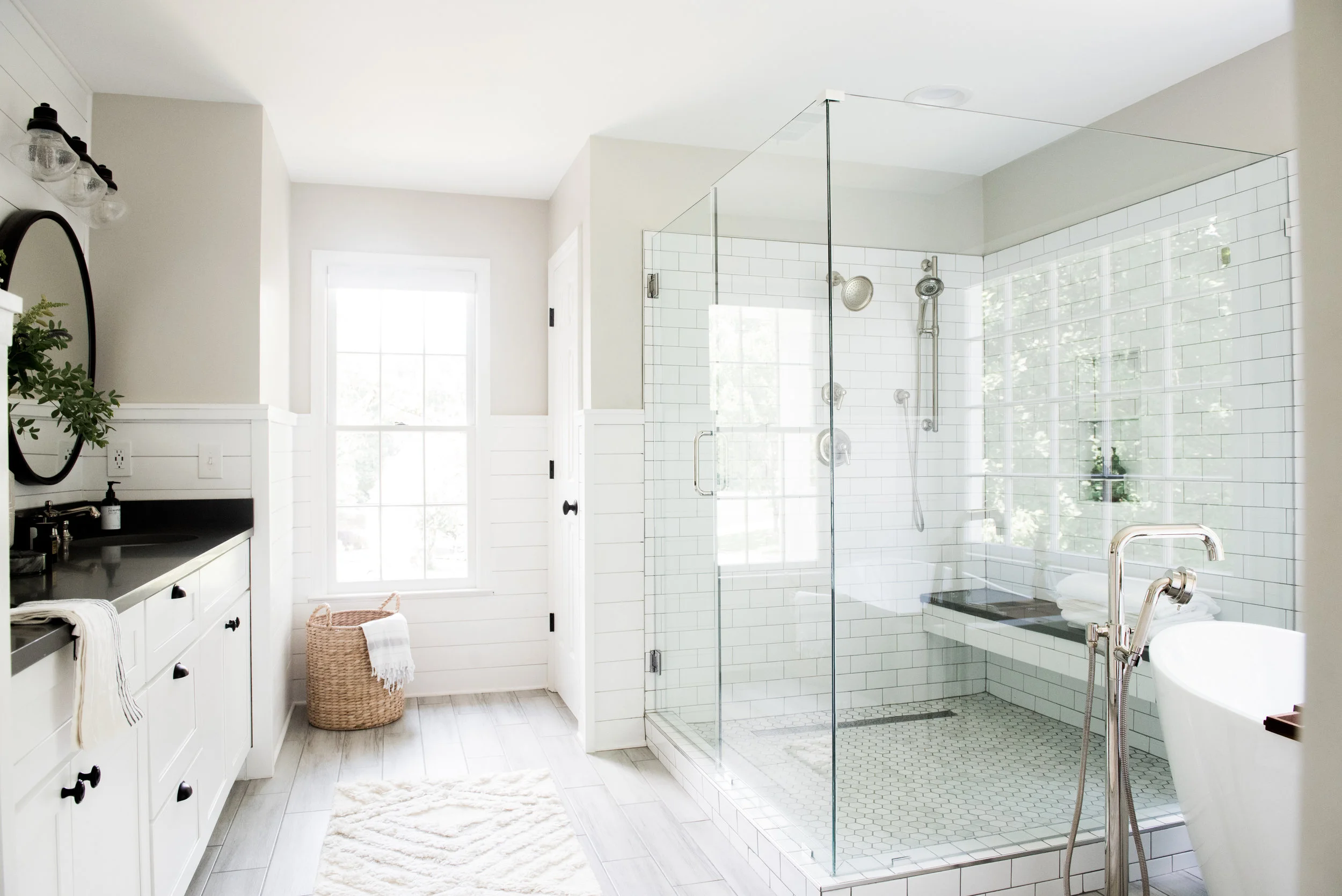 Bright farmhouse-style bathroom with a glass-enclosed shower, black fixtures, white subway tile walls, and a freestanding bathtub.