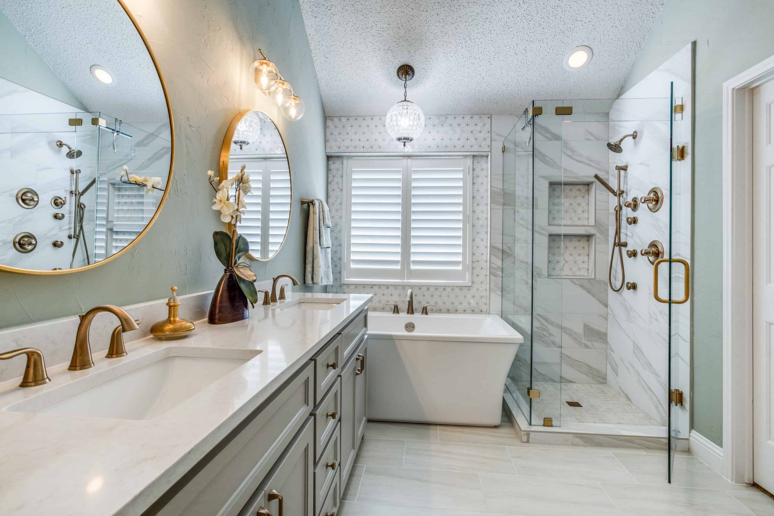 Elegant bathroom with freestanding tub, glass-enclosed shower, gold fixtures, and double vanity with round mirrors.