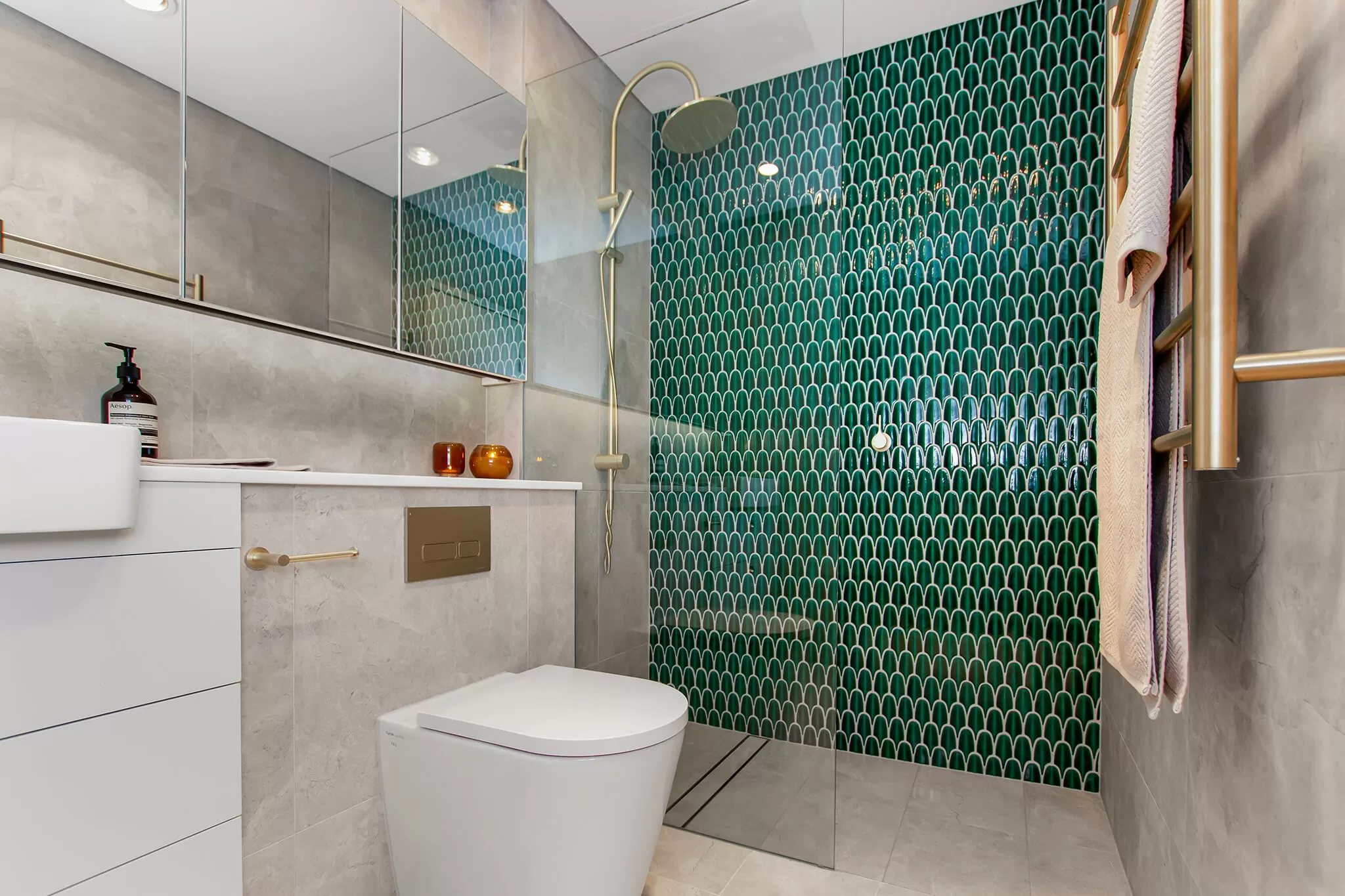 Modern bathroom with green scallop tile shower wall and gold fixtures.