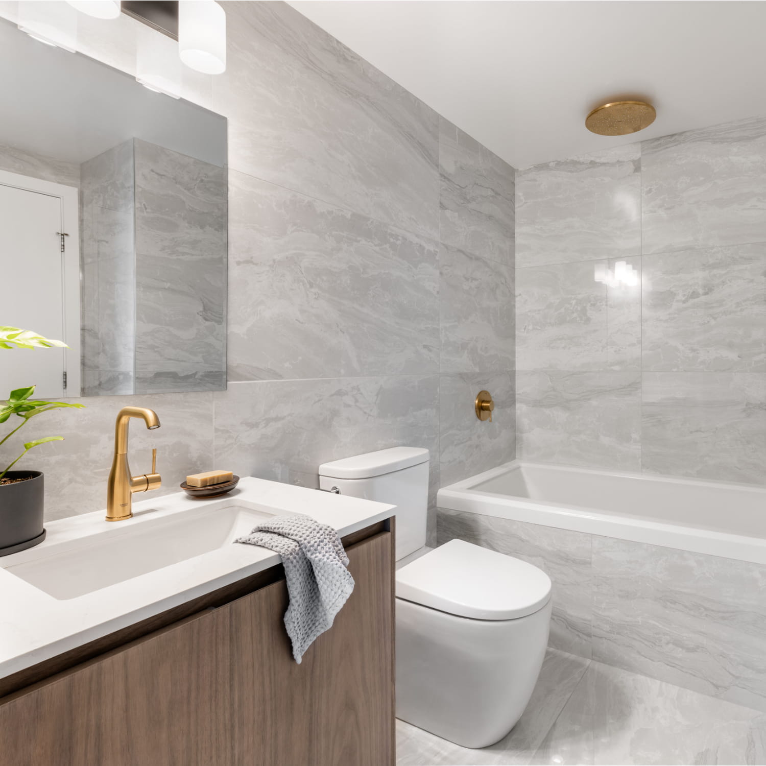 Modern bathroom with gray marble tiles, gold fixtures, and a wooden vanity.