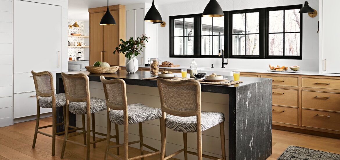 Modern kitchen with black marble waterfall island, natural wood accents, and woven bar stools under black pendant lights.