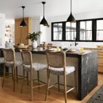 Modern kitchen with black marble waterfall island, natural wood accents, and woven bar stools under black pendant lights.