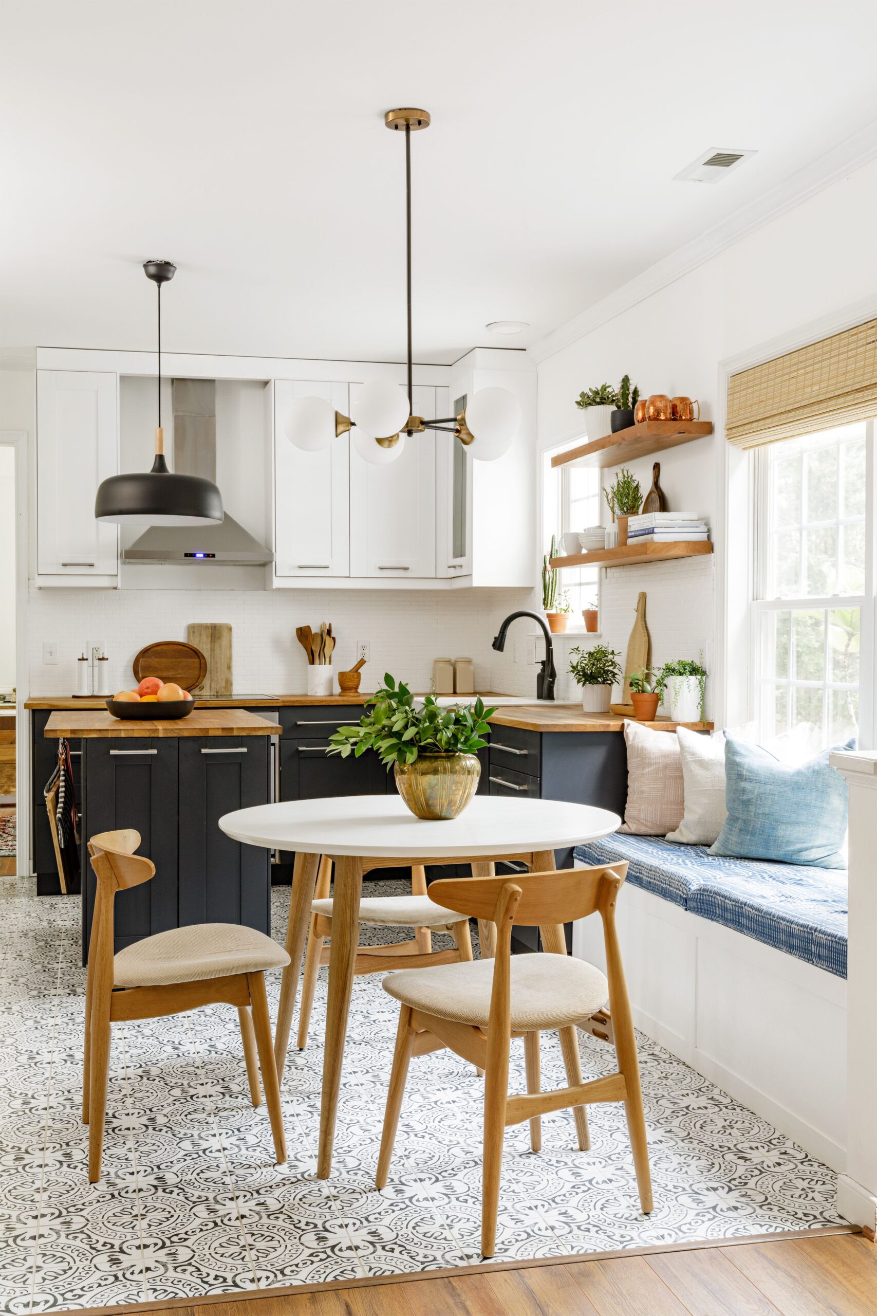 Bright kitchen with white cabinets, black lower cabinetry, wood countertops, and a cozy built-in bench seating area with patterned cushions.