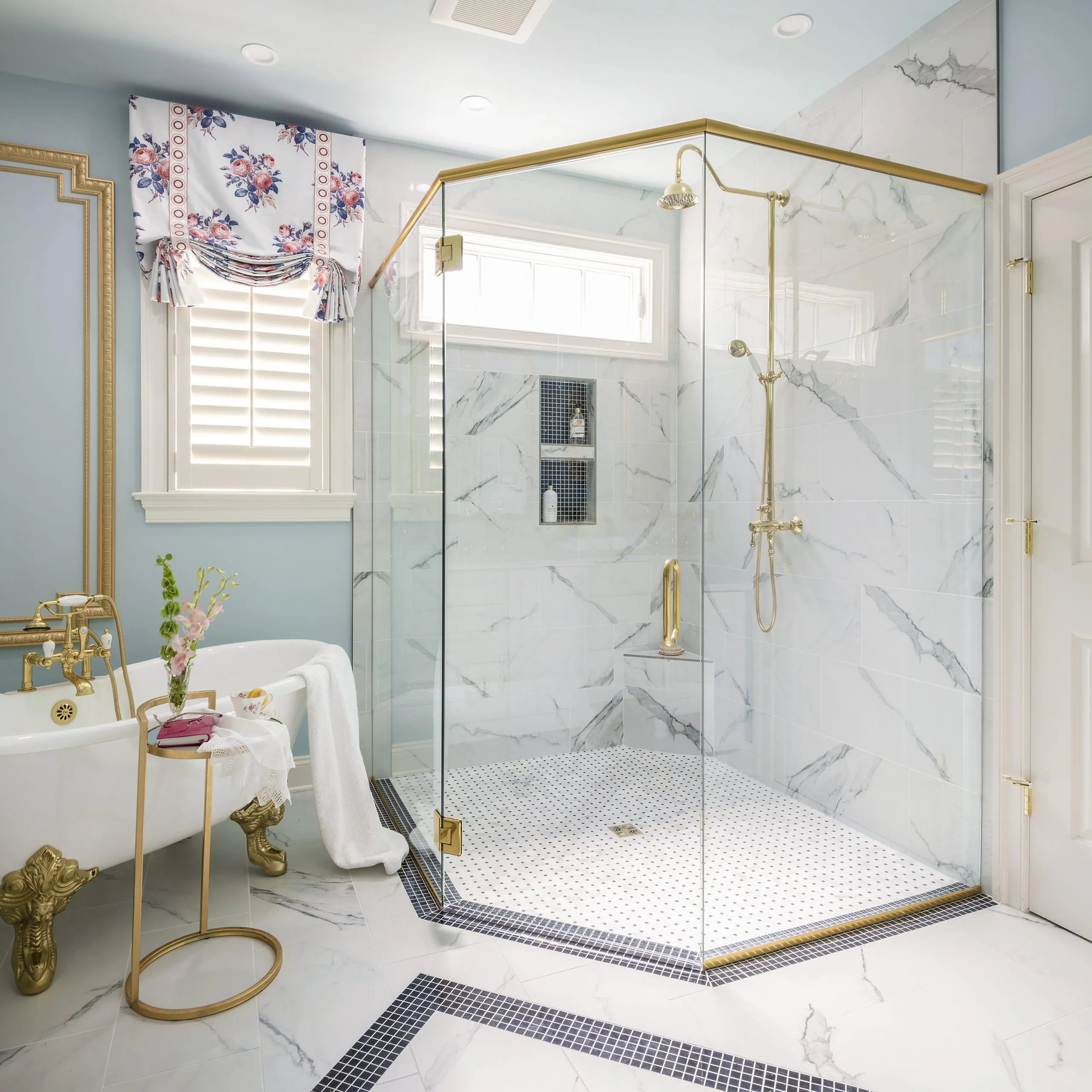 Elegant bathroom with a glass-enclosed shower, marble tile walls, and a clawfoot bathtub with gold accents.
