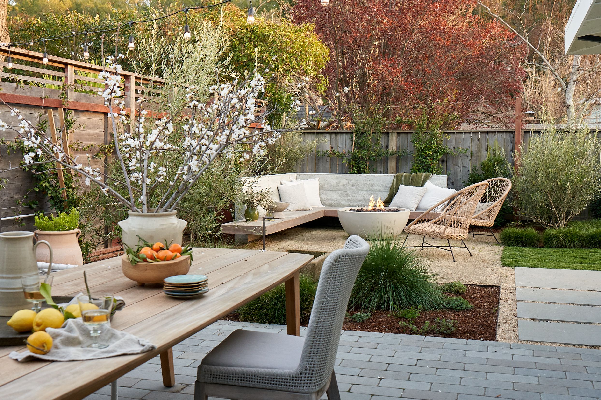 Beautiful backyard with a cozy outdoor seating area, fire pit, dining table with fresh lemons, and string lights creating a warm atmosphere.
