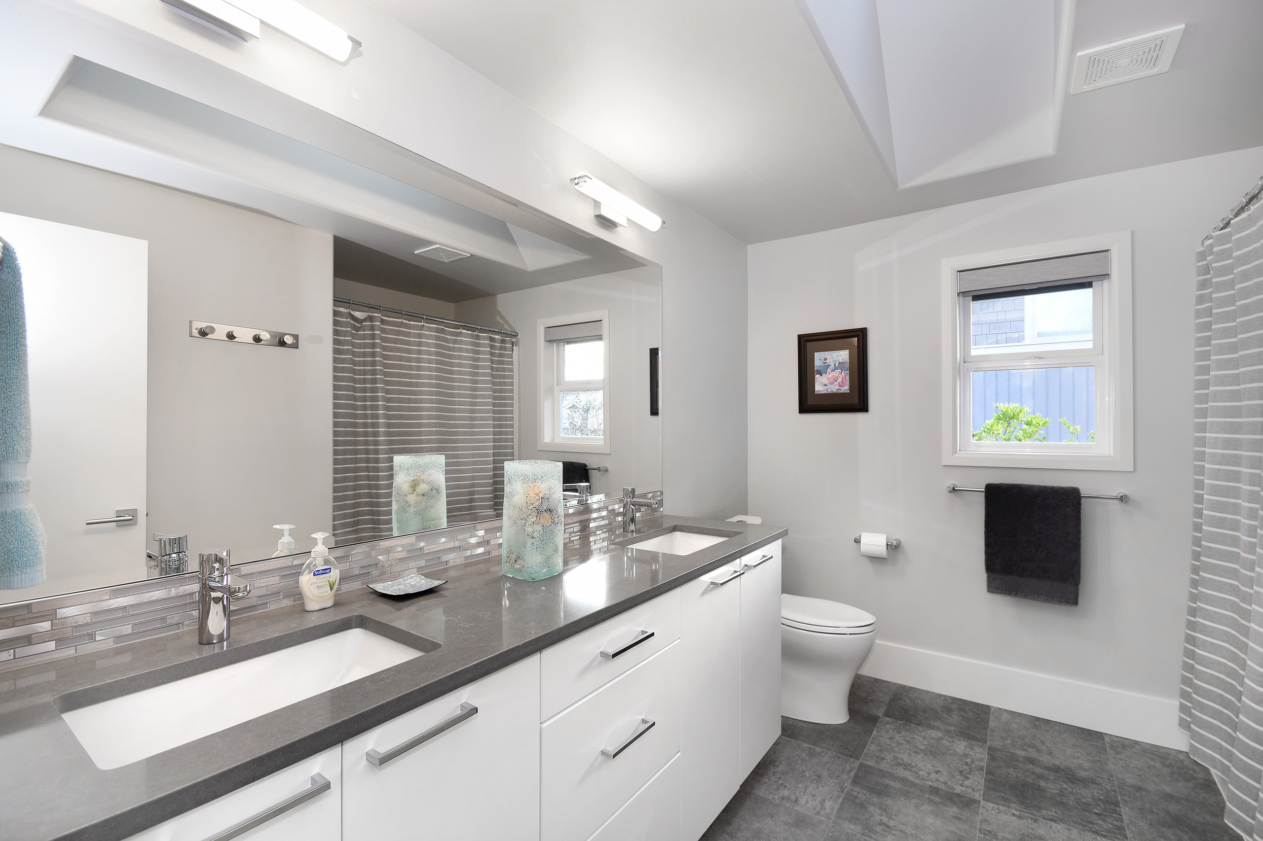Modern bathroom with double-sink vanity, gray countertops, and striped shower curtain.